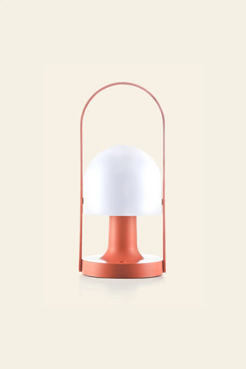 The Marset FollowMe Portable Table Lamp by Marset features a dome-shaped white top, coral base, and matching arched handle, shown against a plain beige background.