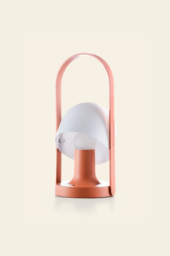 The Marset FollowMe Portable Table Lamp by Marset features a pink base and handle, a white dome-shaped shade, and is rechargeable. Stylish and portable, it’s perfect for any setting. Displayed against a light beige background.
