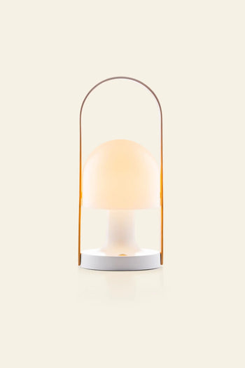 The Marset FollowMe Portable Table Lamp by Marset features a modern, minimalist design with a round frosted bulb, white base, and slim yellow arched handle on a plain beige background.