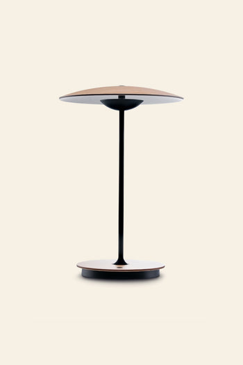 The Marset Ginger 20 M Table Lamp by Marset features a minimalist design with a round, light wood base and matching shade, linked by a sleek black stem—ideal for creating a cosy atmosphere in contemporary homes. Set on a plain beige background.