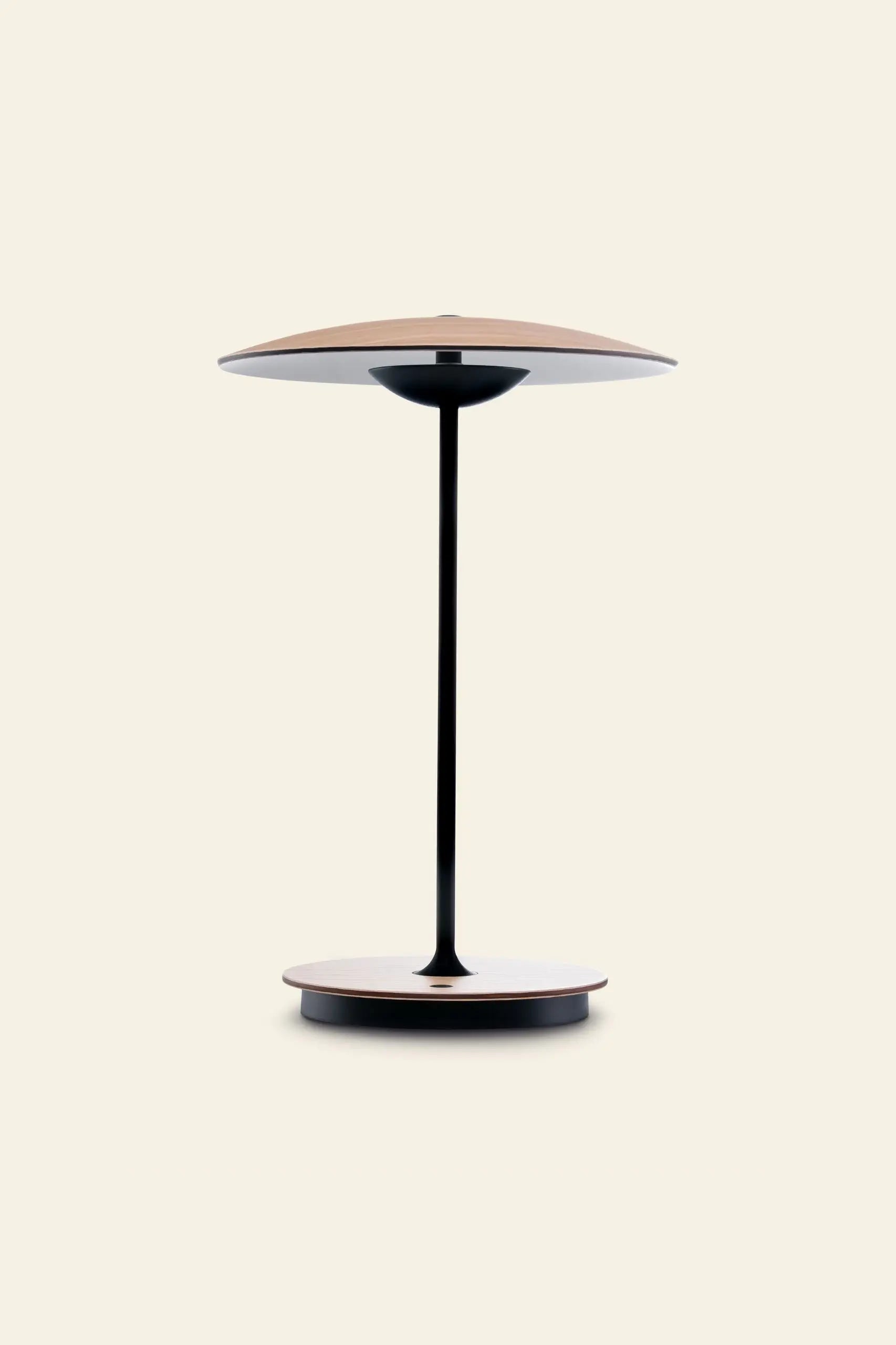 The Marset Ginger 20 M Table Lamp by Marset features a thin black stem, wide flat base, and matching top—ideal for modern home decor and adding a cosy touch to any space with a plain light background.