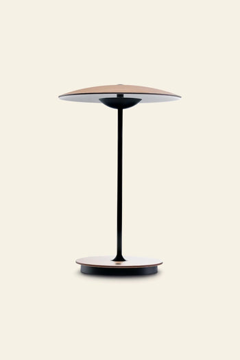 The Marset Ginger 20 M Table Lamp by Marset features a thin black stem, wide flat base, and matching top—ideal for modern home decor and adding a cosy touch to any space with a plain light background.