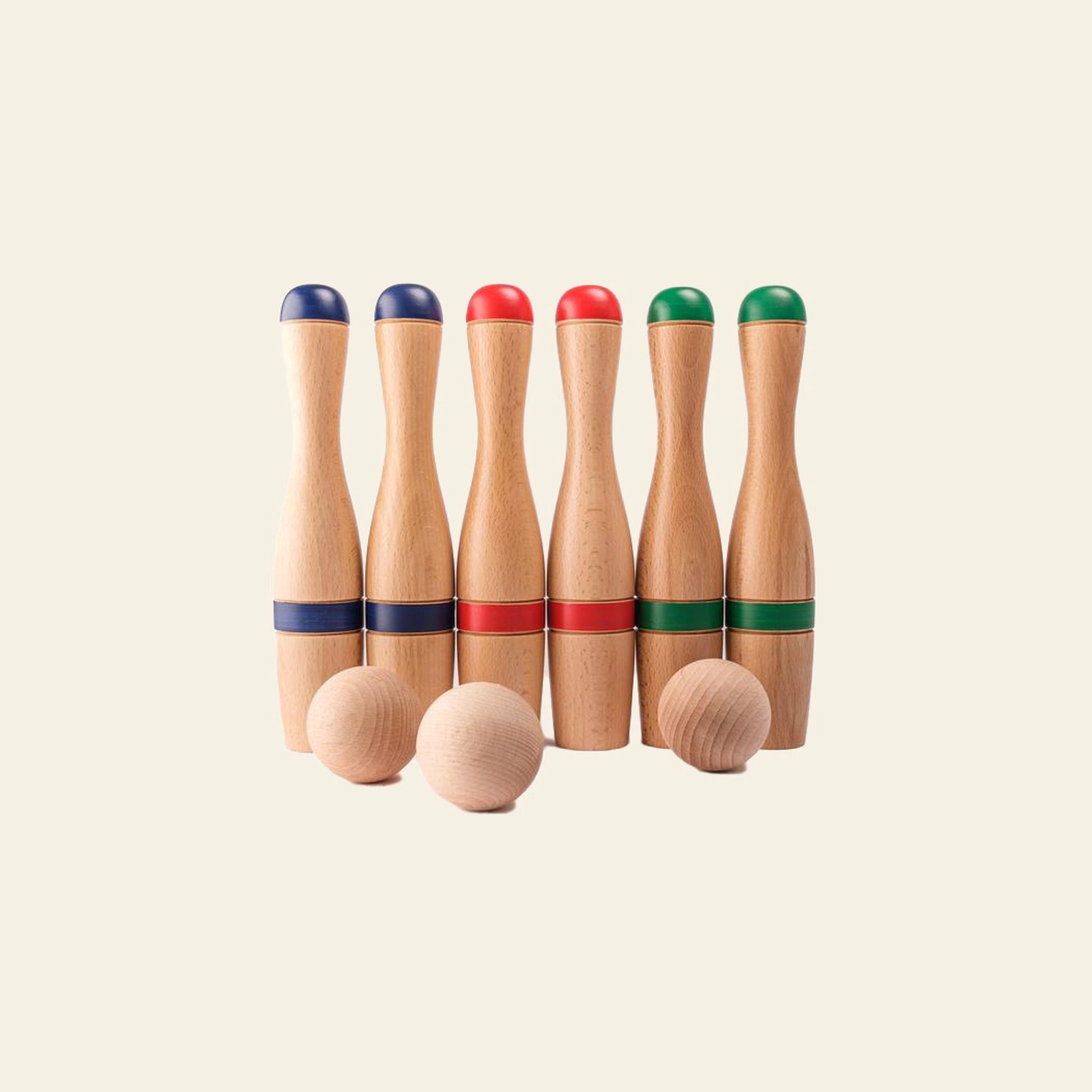The Mora Play Bowling Pins 24cm Set of 6 by Mora Play features six wooden pins with colored tops and bands (two blue, two red, two green) arranged in a row, with two wooden balls in front, all displayed on a plain light background.