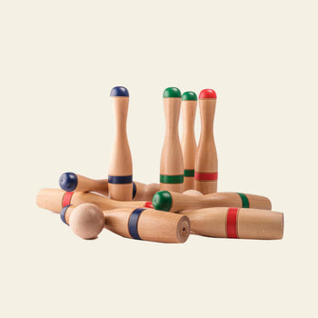 The Mora Play Bowling Pins 24cm Set of 6 by Mora Play features wooden pins with red, green, and blue bands. Some pins are upright while others lie down on a plain, light background.