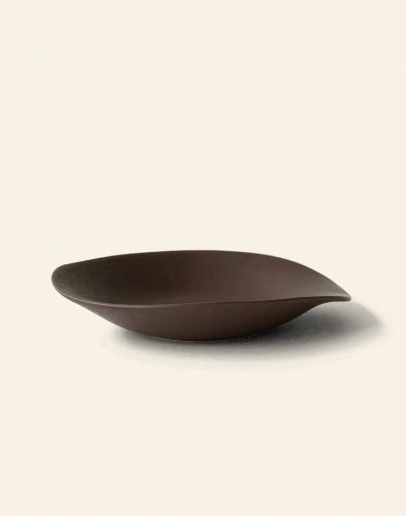 The NR Ceramics HIN Dessert Plate by NR Ceramics is a modern, dark brown ceramic plate with an organic shape and smooth curved edges, shown on a plain light background.