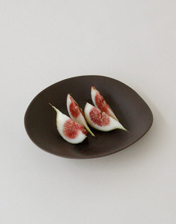 Four slices of fresh fig with red centers and white-green skin are arranged on the NR Ceramics HIN Dessert Plate by NR Ceramics, highlighting their organic shape against a simple, light background.