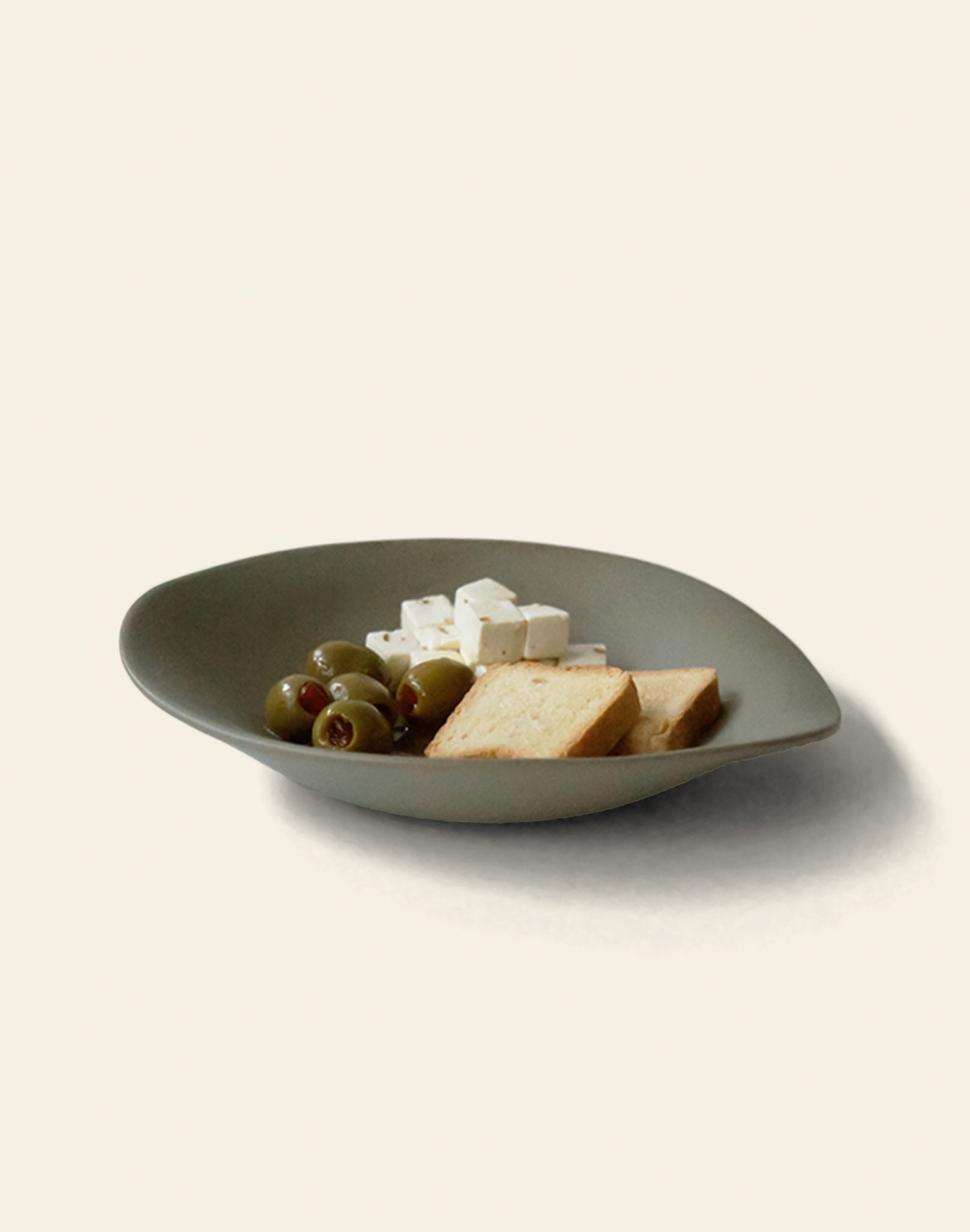 A NR Ceramics HIN Dessert Plate by NR Ceramics, in green, holds green olives, white cheese cubes, and rectangular crackers, arranged neatly on a light beige background.