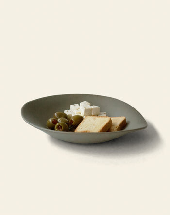 A NR Ceramics HIN Dessert Plate by NR Ceramics, in green, holds green olives, white cheese cubes, and rectangular crackers, arranged neatly on a light beige background.