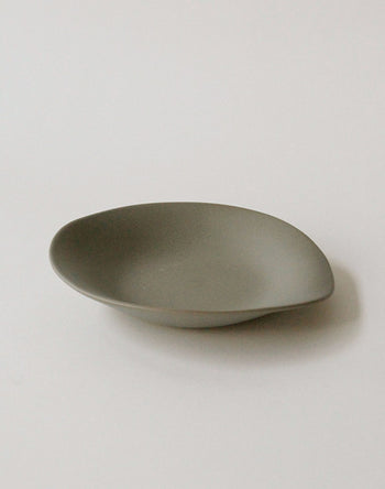 The NR Ceramics HIN Dessert Plate is a minimalist, oval-shaped gray piece with smooth edges and an organic design from NR Ceramics, shown on a plain white background.