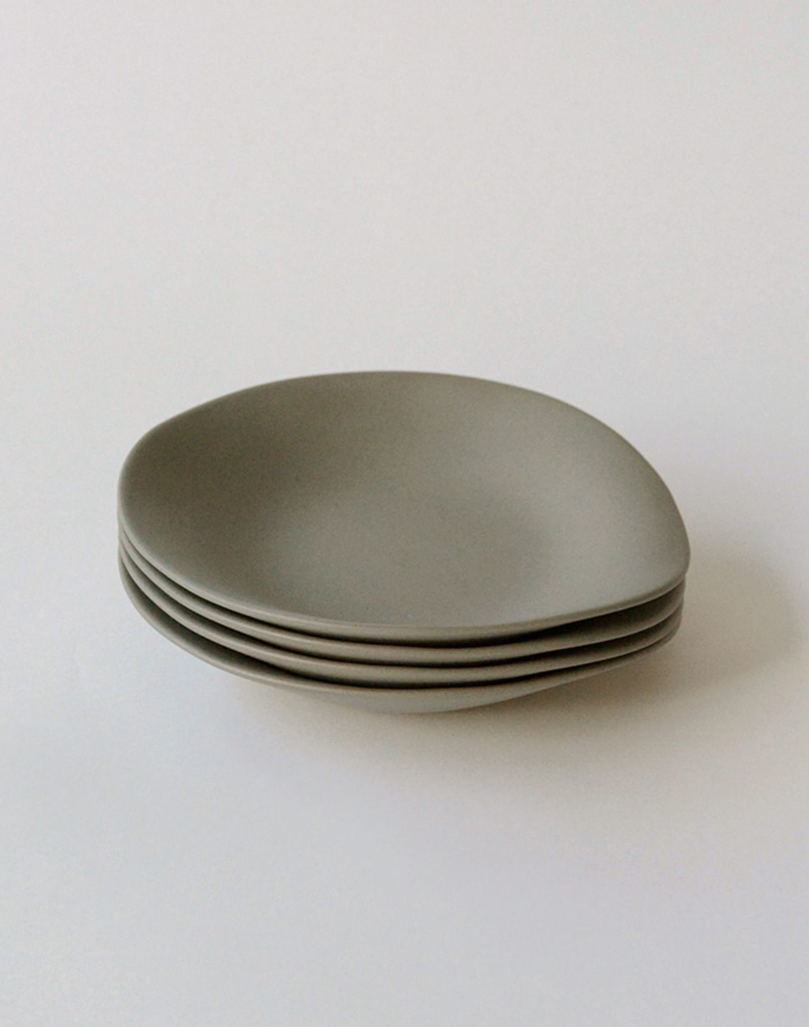 A set of four NR Ceramics HIN Dessert Plates, featuring matte gray, organically shaped round designs with slightly irregular edges, is displayed on a plain white surface.