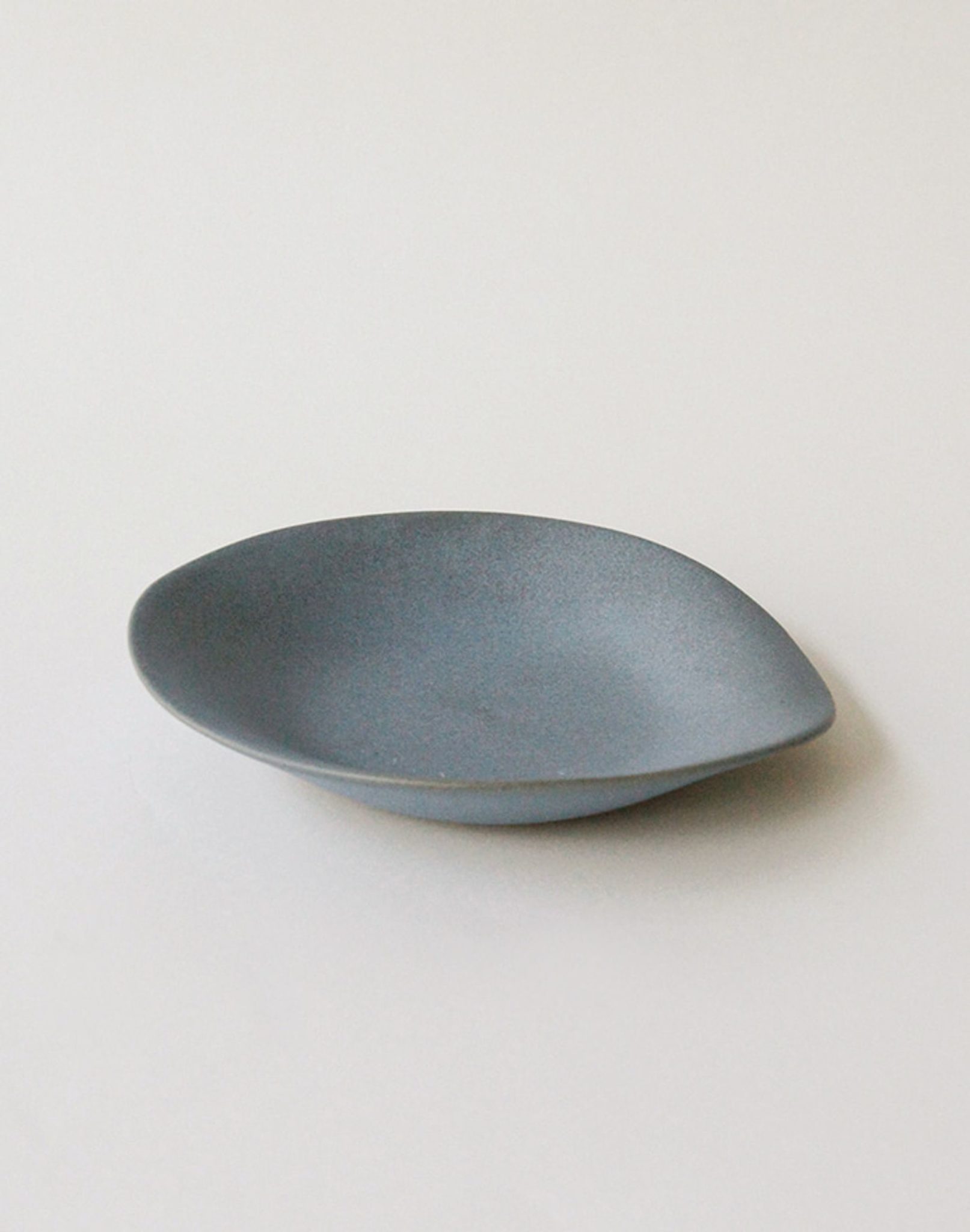 A single NR Ceramics HIN Dessert Plate, featuring a matte blue-gray ceramic finish and an irregular, organic shape, is shown on a plain white background.