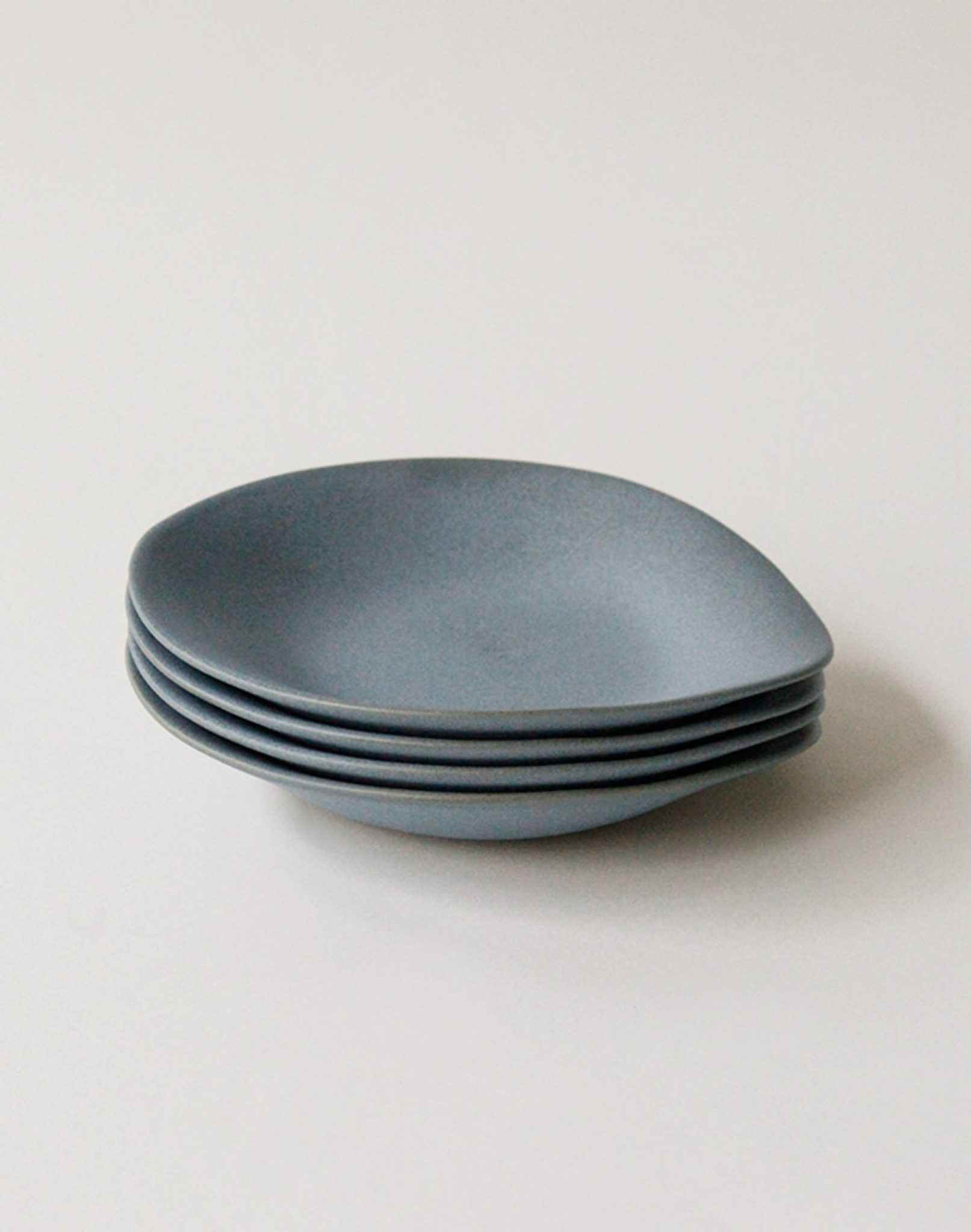 A set of four matte gray NR Ceramics HIN Dessert Plates, each with an organic, slightly irregular shape, displayed on a plain white background.
