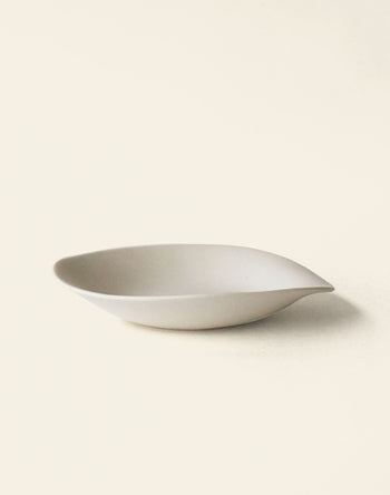 The NR Ceramics HIN Dessert Plate by NR Ceramics features a minimalist white ceramic design with an organic, leaf-inspired shape and smooth, curved edges, shown against a light neutral backdrop.