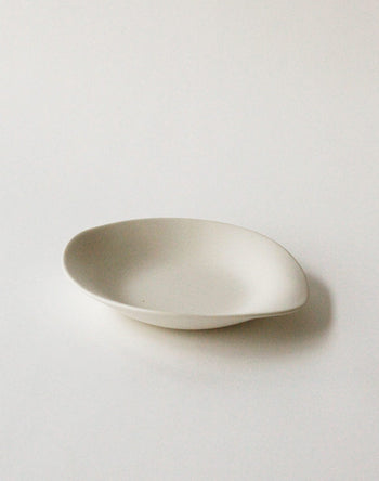 The NR Ceramics HIN Dessert Plate by NR Ceramics features an off-white finish and a slightly irregular oval shape. This plain, shallow plate from the Hin collection is shown resting on a white surface.