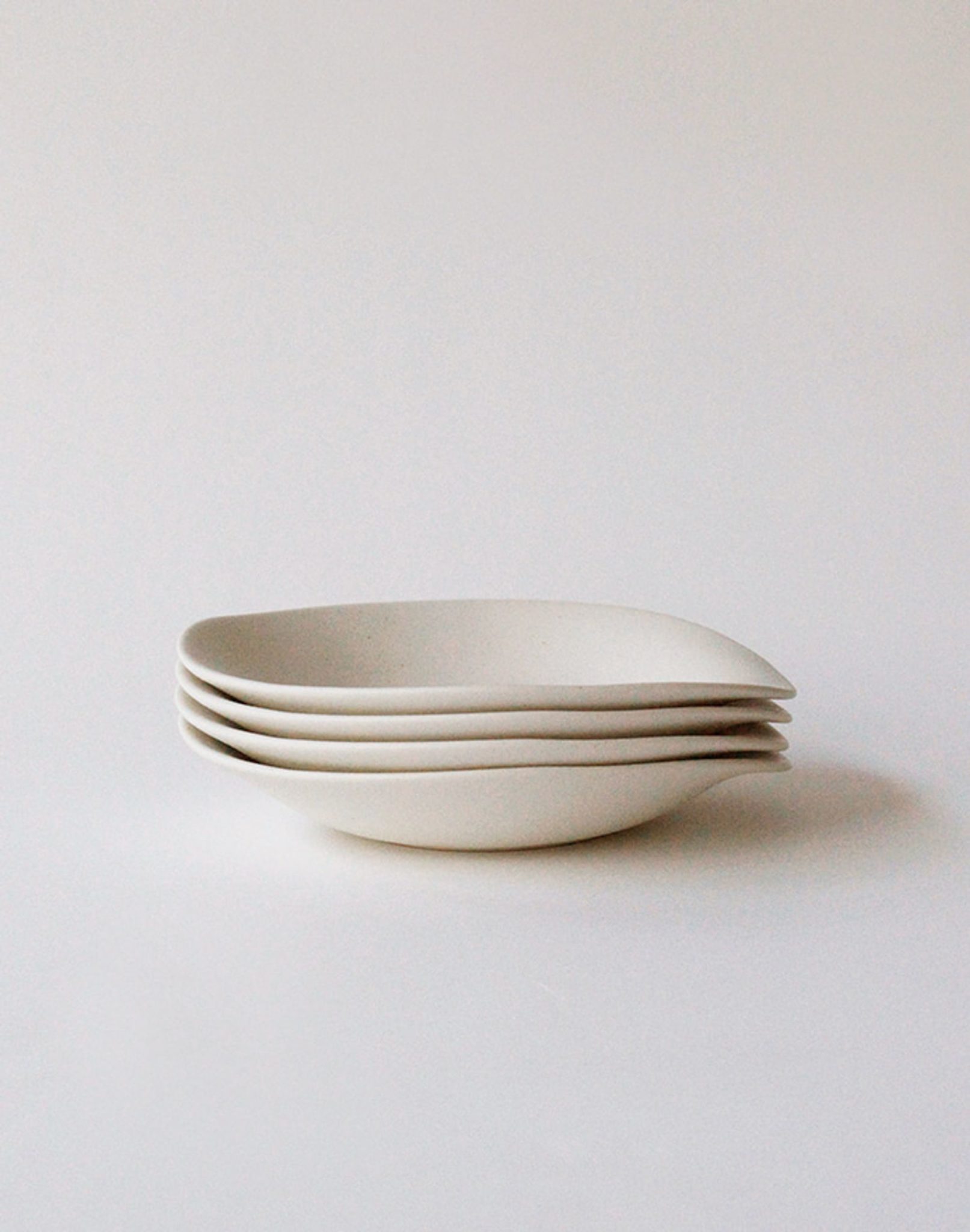 Four NR Ceramics HIN Dessert Plates, featuring a minimalist, white, organic design, are stacked neatly on a plain white background.