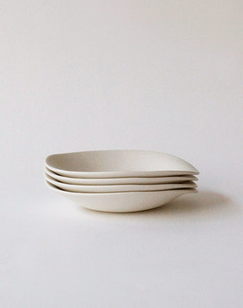 Four NR Ceramics HIN Dessert Plates, featuring a minimalist, white, organic design, are stacked neatly on a plain white background.
