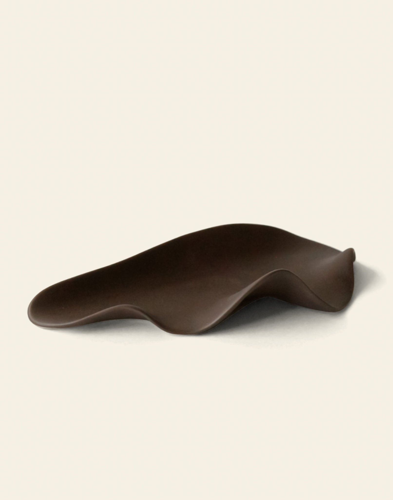 The NR Ceramics HIN Leaf Plate by NR Ceramics features a dark brown, abstract design with smooth, wavy edges and an organic shape, making it a striking, multi-functional tableware piece against a plain light background.