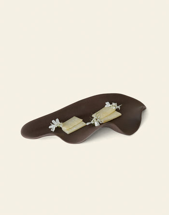 The NR Ceramics HIN Leaf Plate from NR Ceramics displays two rectangular cheese slices, topped with edible white flowers and herb sprigs, highlighting its multi-functional tableware design against a plain light backdrop.
