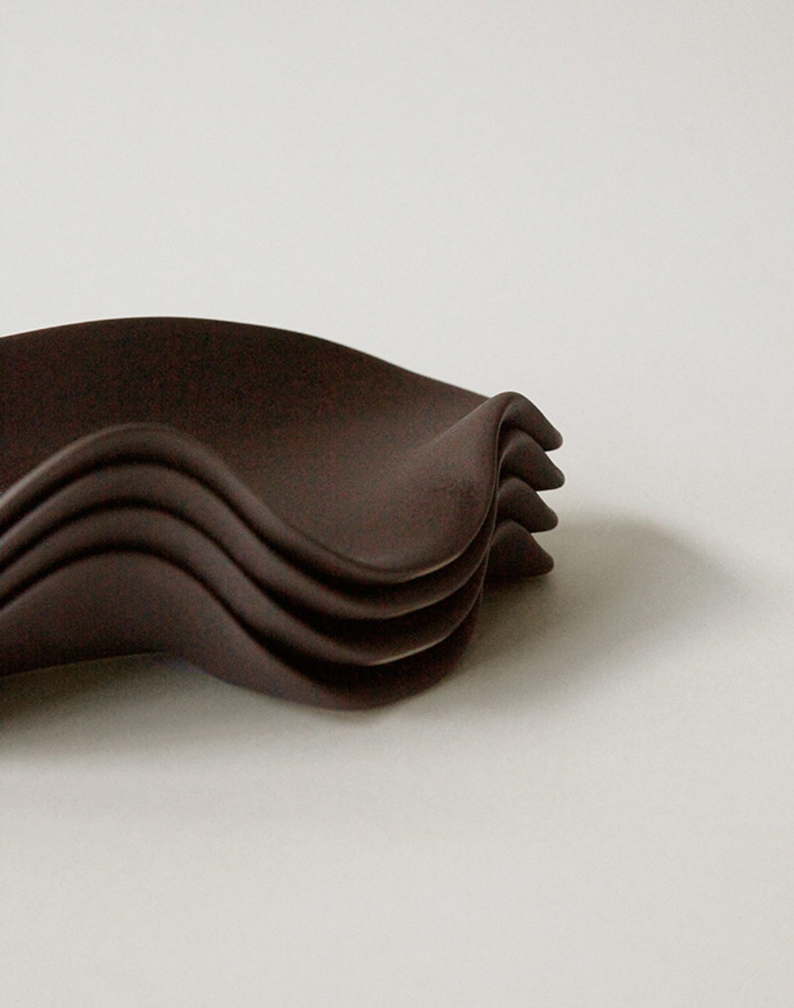 A stack of NR Ceramics HIN Leaf Plates, featuring dark, wavy edges, is arranged on a plain light surface with the overlapping plates forming a layered, sculptural look.
