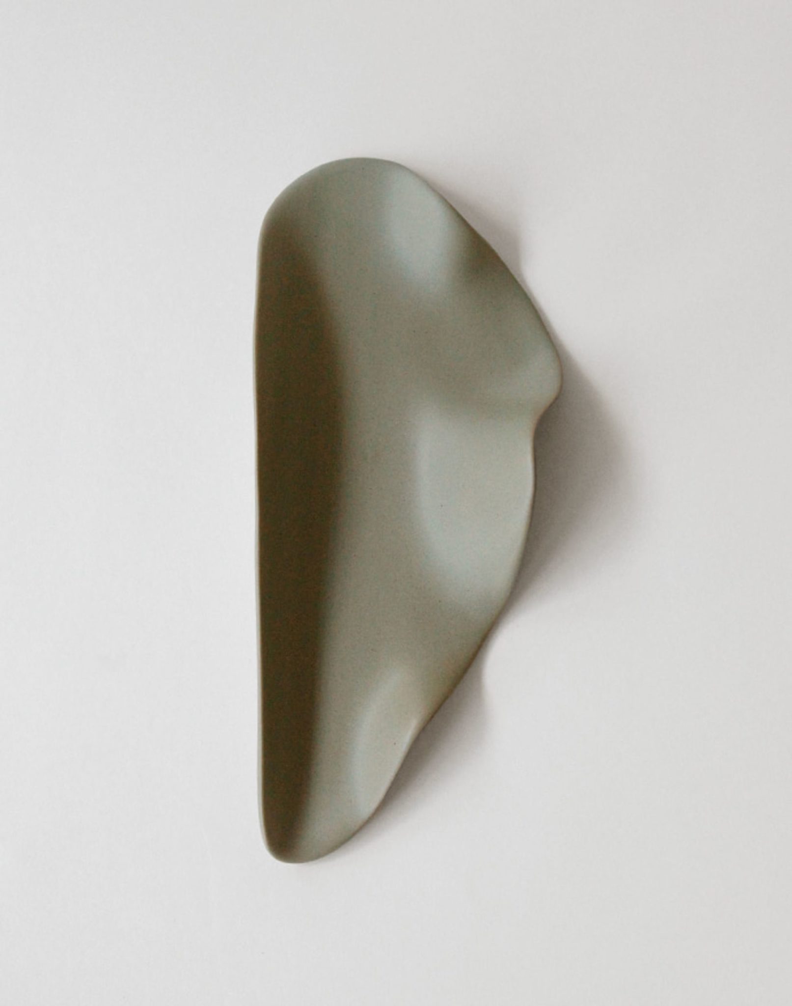 The NR Ceramics HIN Leaf Plate features a smooth, abstract form with an organic shape and matte gray-green finish. This versatile ceramic dish by NR Ceramics adds modern style to your tableware. Shown on a plain white background.