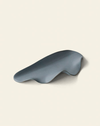 A smooth, abstract gray object with an organic shape sits on a plain background—reminiscent of the NR Ceramics HIN Leaf Plate by NR Ceramics, known for its sculptural form and versatile tableware design.