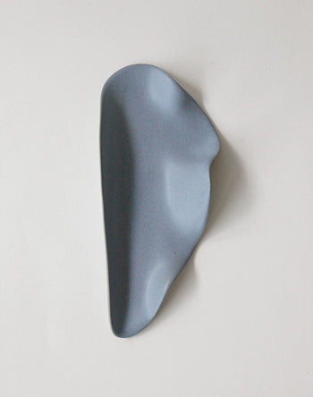 The NR Ceramics HIN Leaf Plate, a blue ceramic piece with smooth contours and gentle curves, features an abstract, organic shape. This versatile tableware item is set against a plain white background.