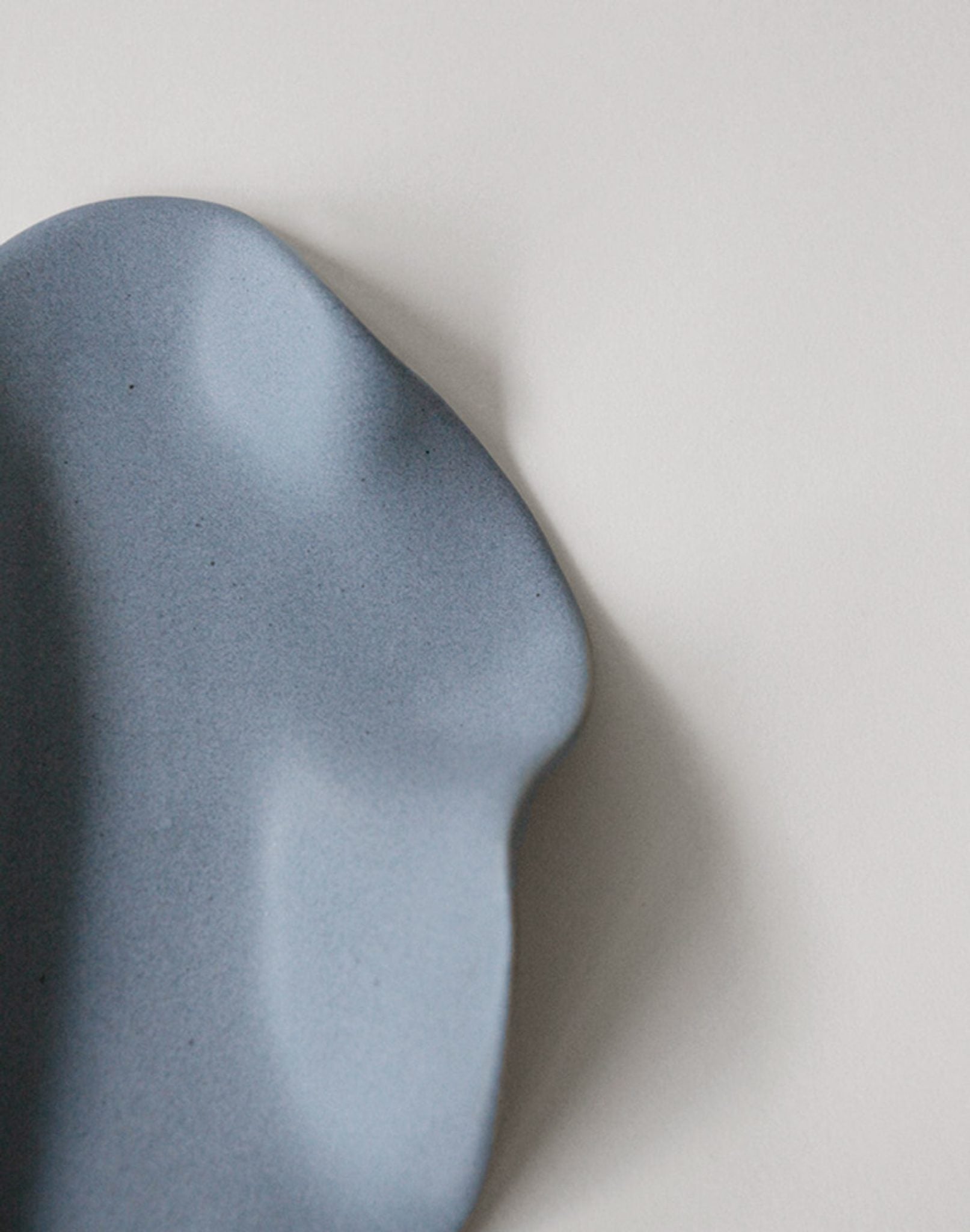 A close-up of the NR Ceramics HIN Leaf Plate by NR Ceramics, featuring a matte blue finish, organic wavy edges, and smooth texture—ideal as versatile tableware for any setting.