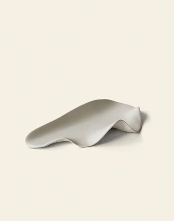 The NR Ceramics HIN Leaf Plate by NR Ceramics is a smooth, white ceramic piece with gentle curves and an abstract, undulating shape, offering a multi-functional design that elevates modern tableware on any setting.