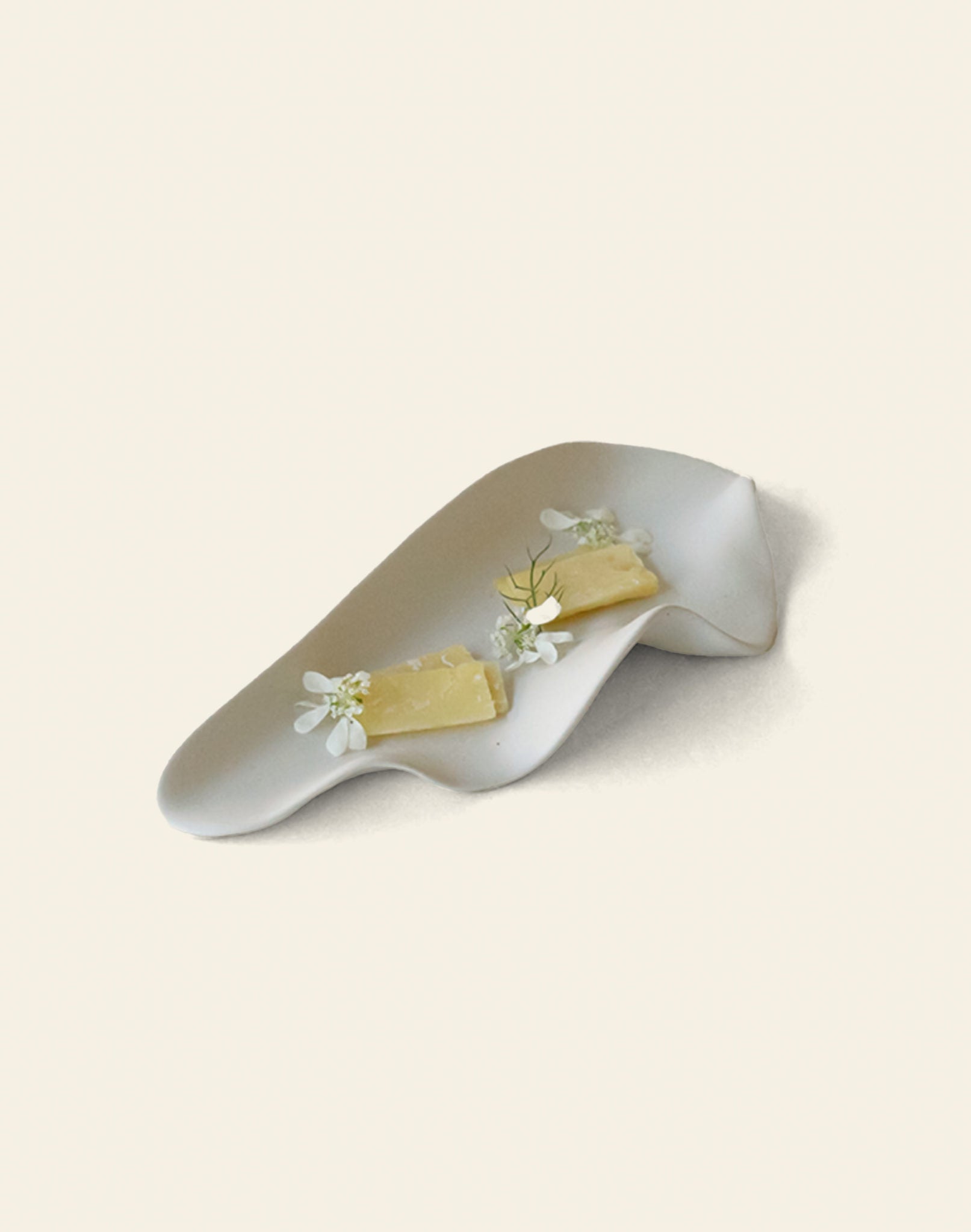 The NR Ceramics HIN Leaf Plate by NR Ceramics displays two cheeses adorned with white flowers and dill, demonstrating elegant and versatile tableware against a plain cream background.
