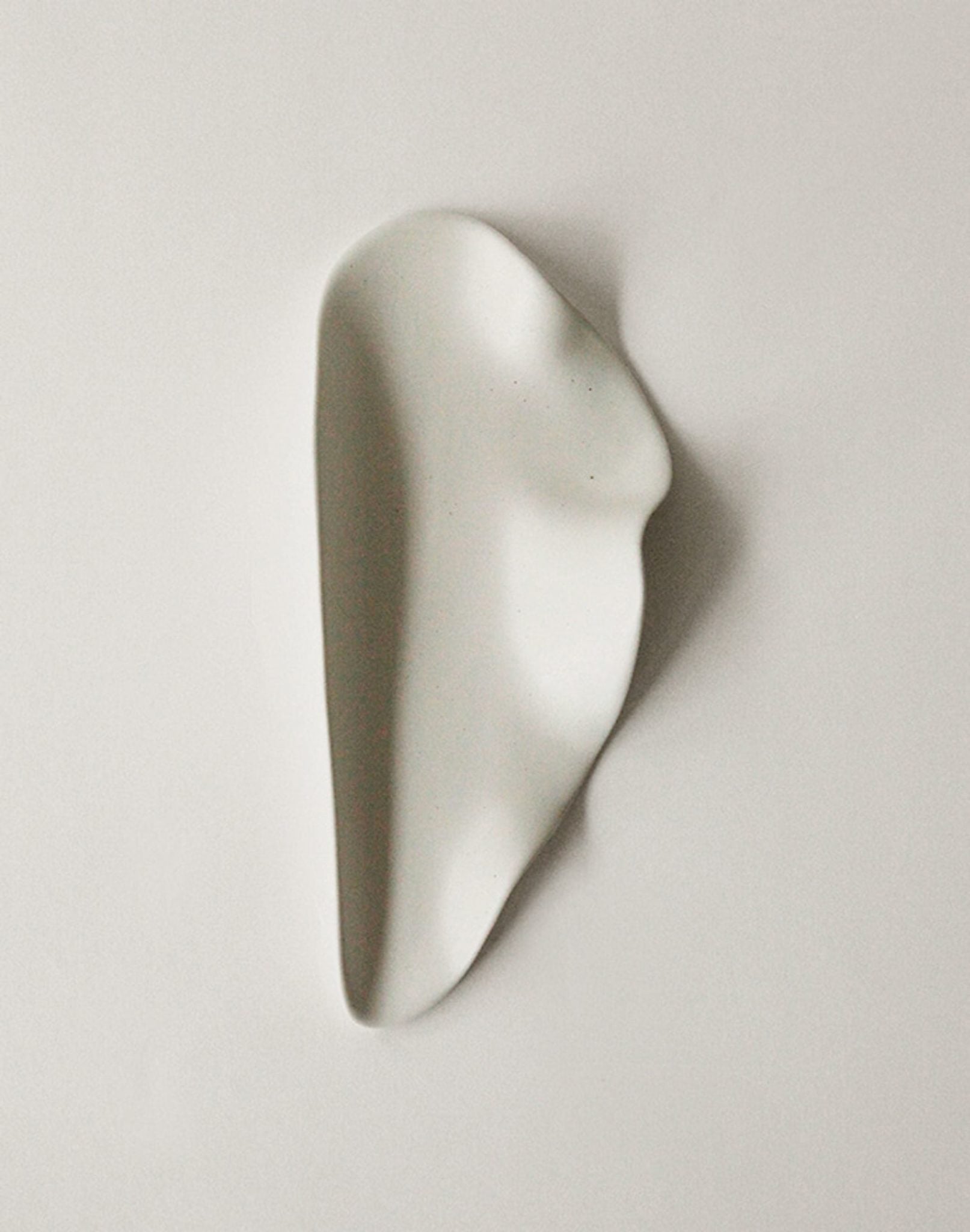 The NR Ceramics HIN Leaf Plate by NR Ceramics is a smooth, white ceramic piece with an irregular, organic shape—abstract and minimalist—displayed on a plain light background.