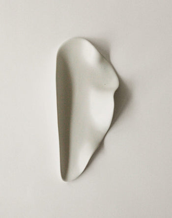 The NR Ceramics HIN Leaf Plate by NR Ceramics is a smooth, white ceramic piece with an irregular, organic shape—abstract and minimalist—displayed on a plain light background.