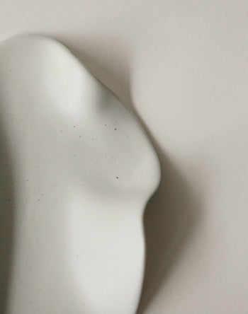 The NR Ceramics HIN Leaf Plate, by NR Ceramics, is a smooth, white ceramic piece with gentle curves and soft shadows on a light surface, echoing the organic elegance of abstract sculpture and multi-functional tableware.