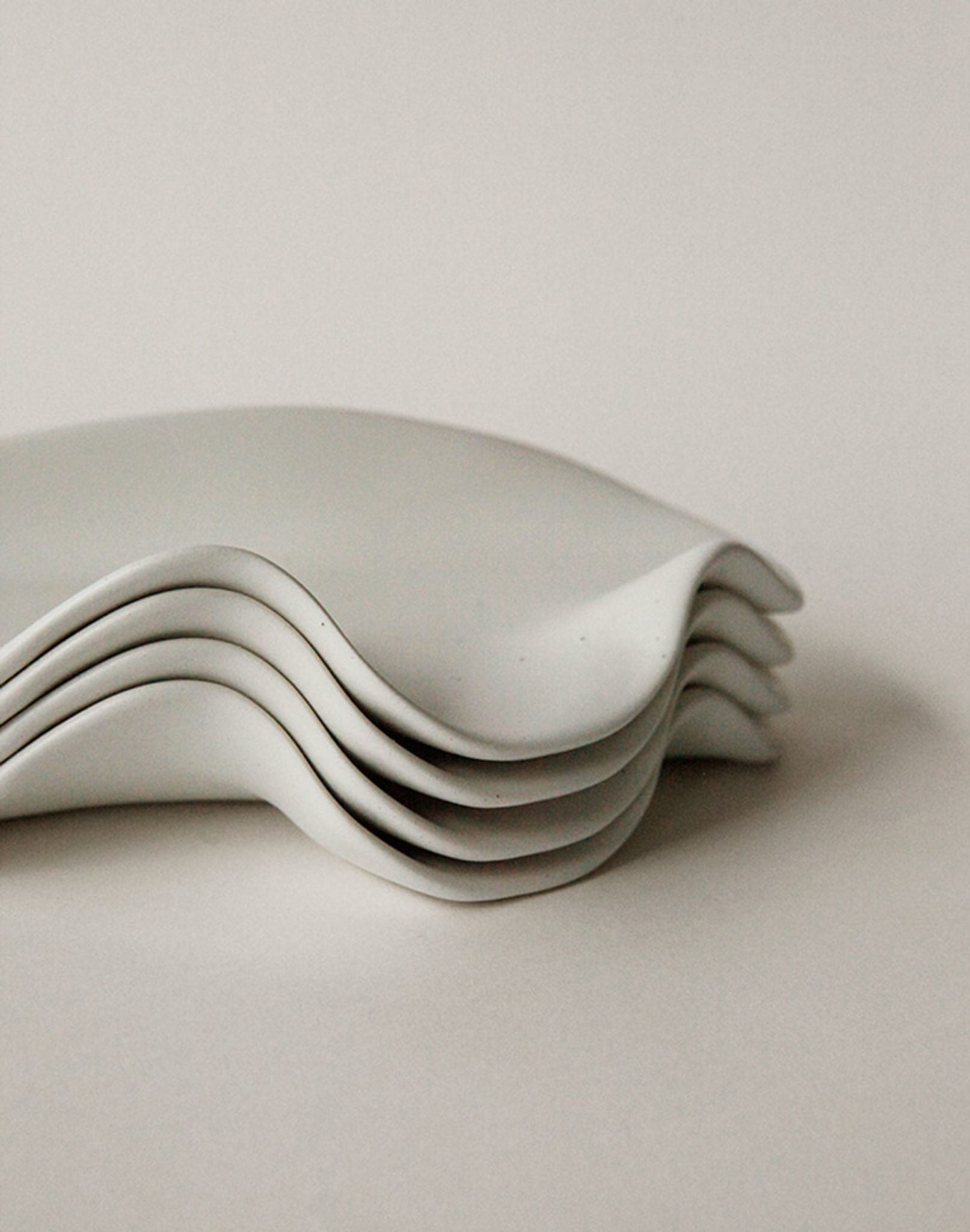 A close-up shows four NR Ceramics HIN Leaf Plates with elegant wavy edges stacked together, highlighting this stylish and versatile tableware set against a plain, light background.
