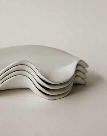 A close-up shows four NR Ceramics HIN Leaf Plates with elegant wavy edges stacked together, highlighting this stylish and versatile tableware set against a plain, light background.