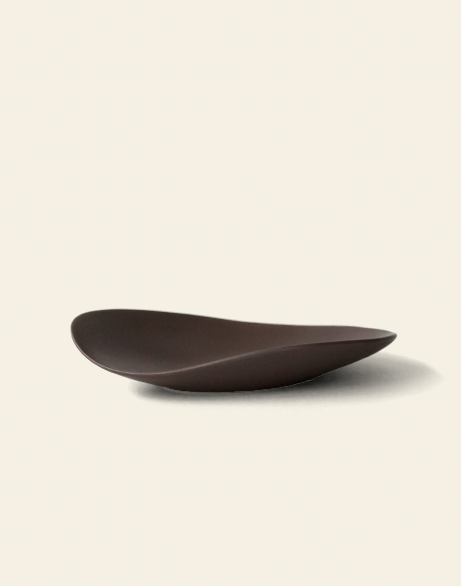 The NR Ceramics HIN Pebble Plate S is a dark brown, modern ceramic plate with an asymmetrical, smooth wavy design, photographed on a plain off-white background.