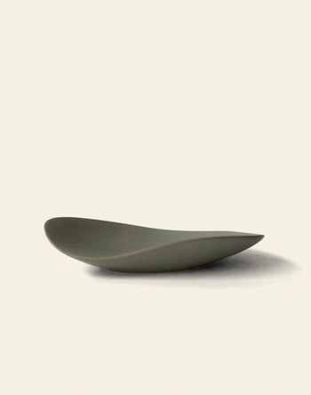 The NR Ceramics HIN Pebble Plate S features a minimalist, shallow design in matte gray with smooth, curved edges—an elegant addition to contemporary tableware, shown on a plain off-white background.