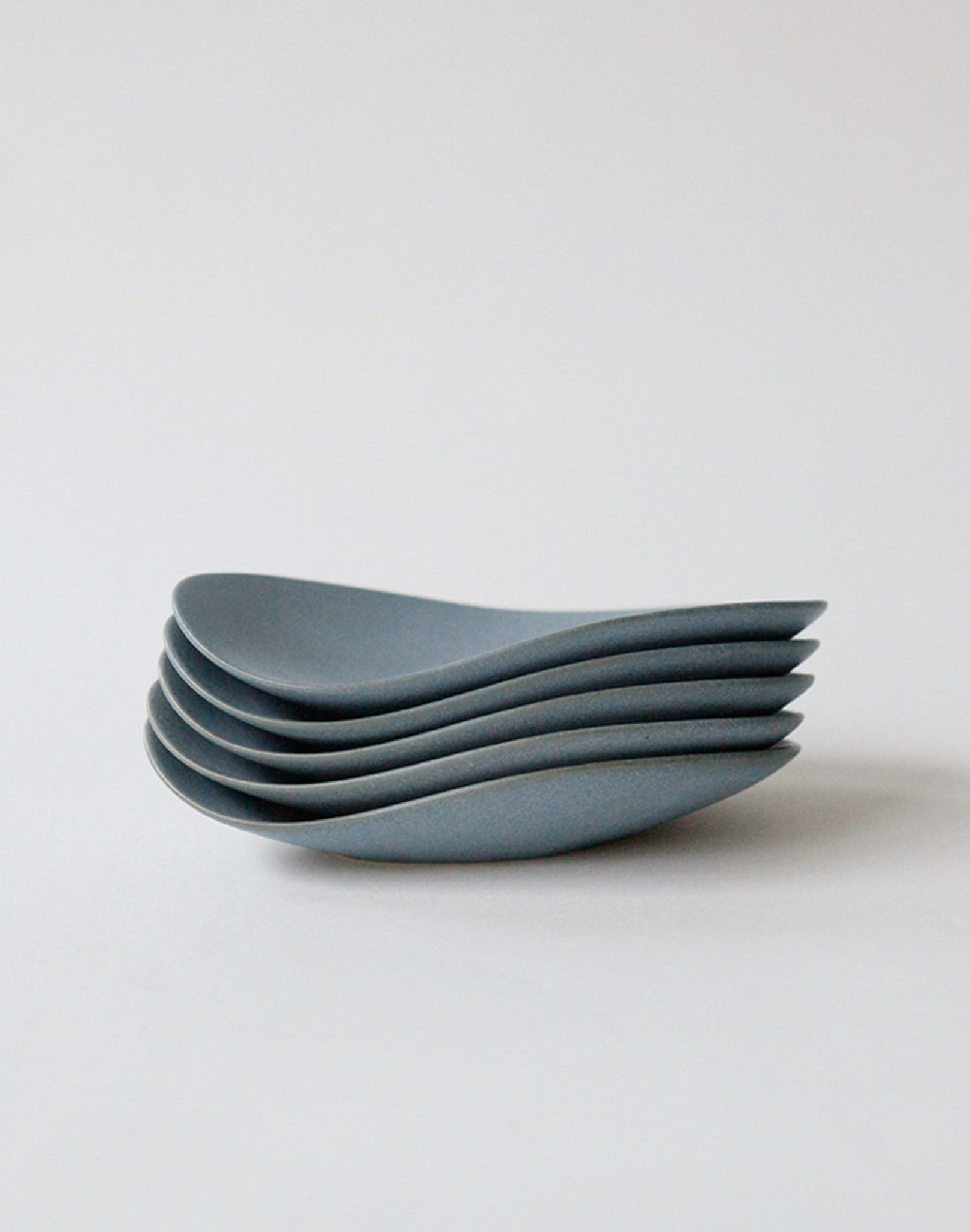 A stack of five NR Ceramics HIN Pebble Plate S pieces is arranged neatly on a plain white background, showcasing the brand’s minimalist design with smooth, curved lines and overlapping edges.