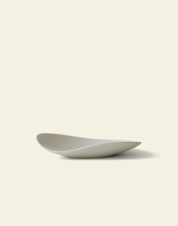 The NR Ceramics HIN Pebble Plate S is a minimalist white tableware piece with smooth, curved edges, shown on a plain light background and casting a soft shadow to the right.