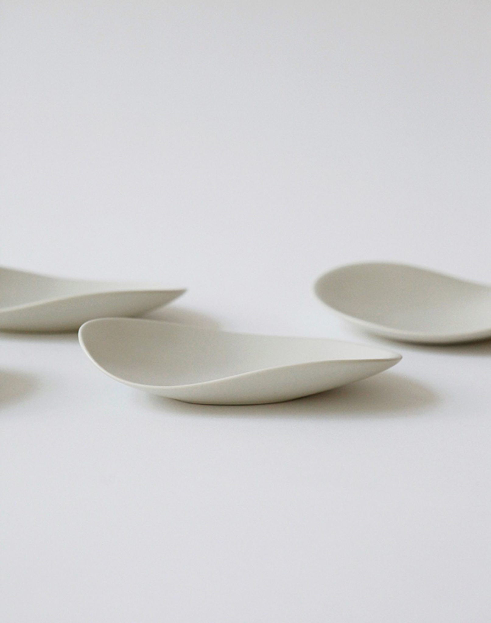 Four NR Ceramics HIN Pebble Plate S pieces, featuring a minimalist white ceramic design with smooth, curved edges, are arranged on a plain white background for a clean, modern tableware look.