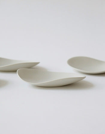 Four NR Ceramics HIN Pebble Plate S pieces, featuring a minimalist white ceramic design with smooth, curved edges, are arranged on a plain white background for a clean, modern tableware look.