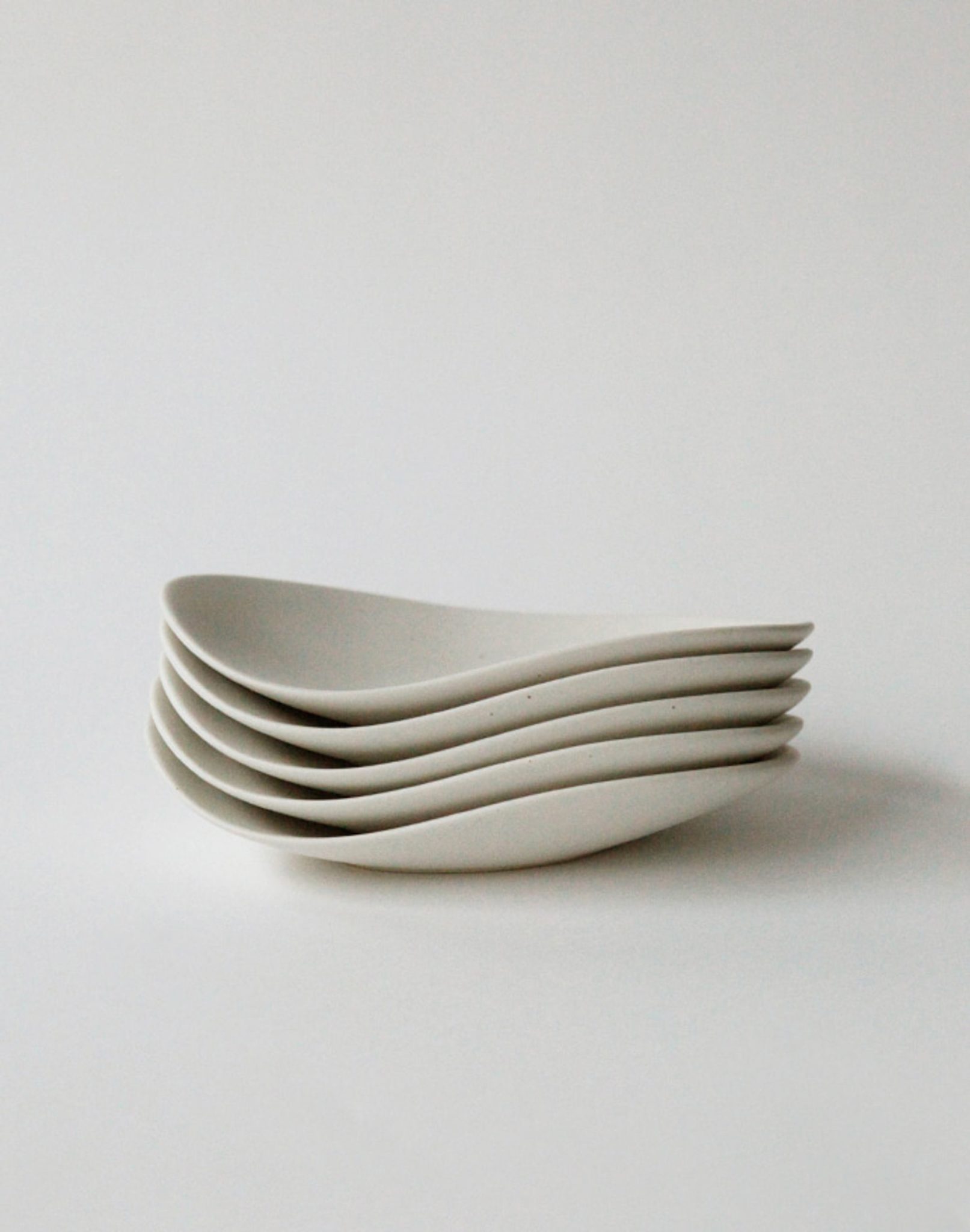 A stack of five NR Ceramics HIN Pebble Plate S bowls, each minimalist white ceramic with smooth curved edges, arranged on a plain light background—perfect for elevating your tableware ensemble.
