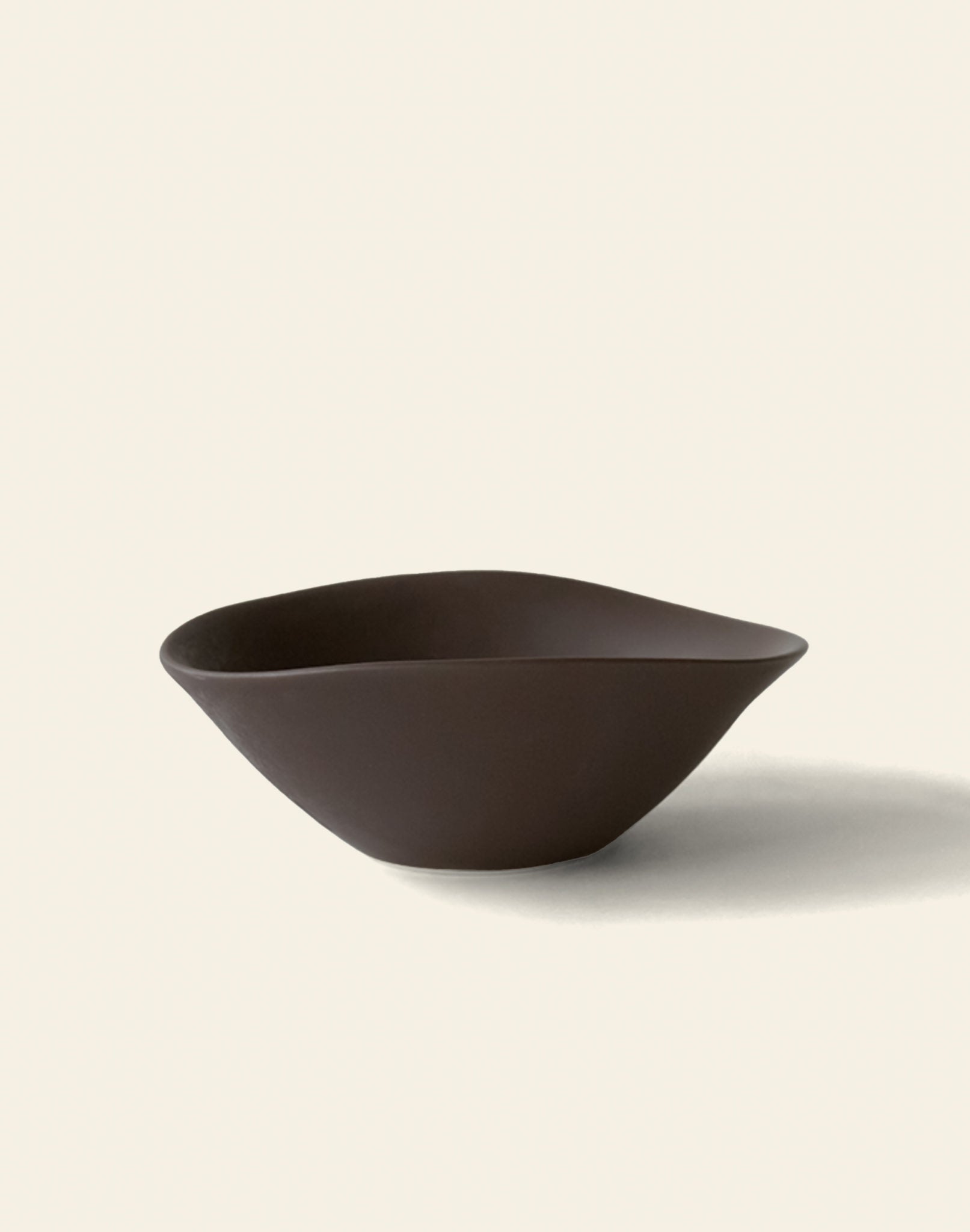 The NR Ceramics HIN Soup Bowl, a dark brown modern piece with an asymmetrical organic shape from NR Ceramics, rests on a plain light background and casts a soft shadow to the right.