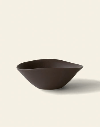 The NR Ceramics HIN Soup Bowl, a dark brown modern piece with an asymmetrical organic shape from NR Ceramics, rests on a plain light background and casts a soft shadow to the right.