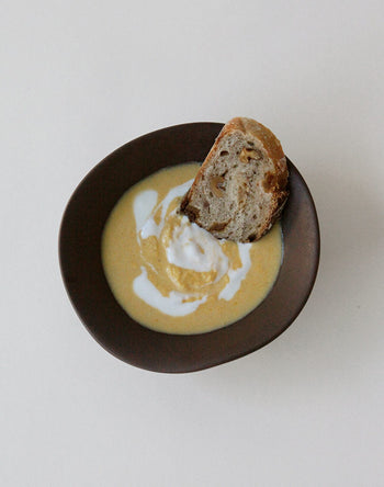 A NR Ceramics HIN Soup Bowl by NR Ceramics, filled with creamy soup and topped with a swirl of white cream, is paired with rustic bread to highlight this versatile tableware against a plain white background.