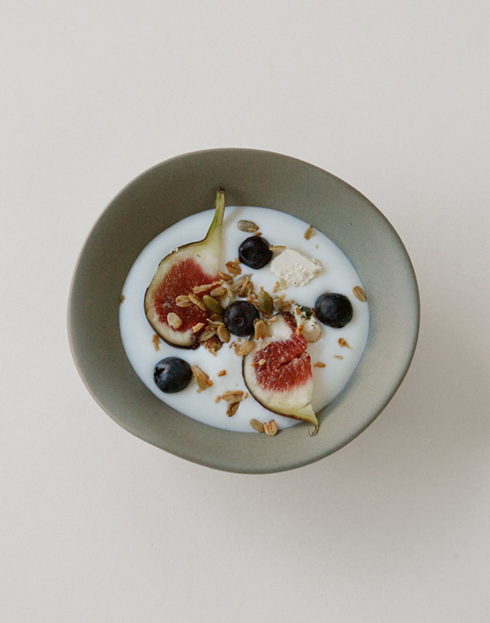 The NR Ceramics HIN Soup Bowl by NR Ceramics holds yogurt topped with figs, blueberries, granola, and seeds, displayed on a light-colored surface.