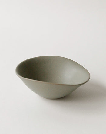 The NR Ceramics HIN Soup Bowl, a small matte gray ceramic piece with an organic, irregular shape from NR Ceramics, rests on a plain white surface.