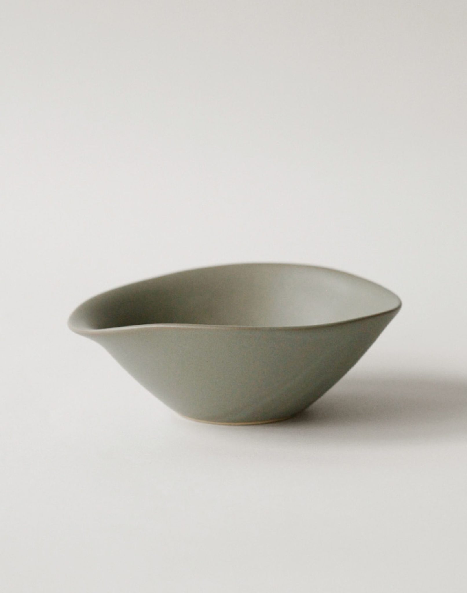 The NR Ceramics HIN Soup Bowl is a matte, olive-green ceramic piece with an asymmetric, organic shape—versatile tableware from NR Ceramics, ideal for modern dining.