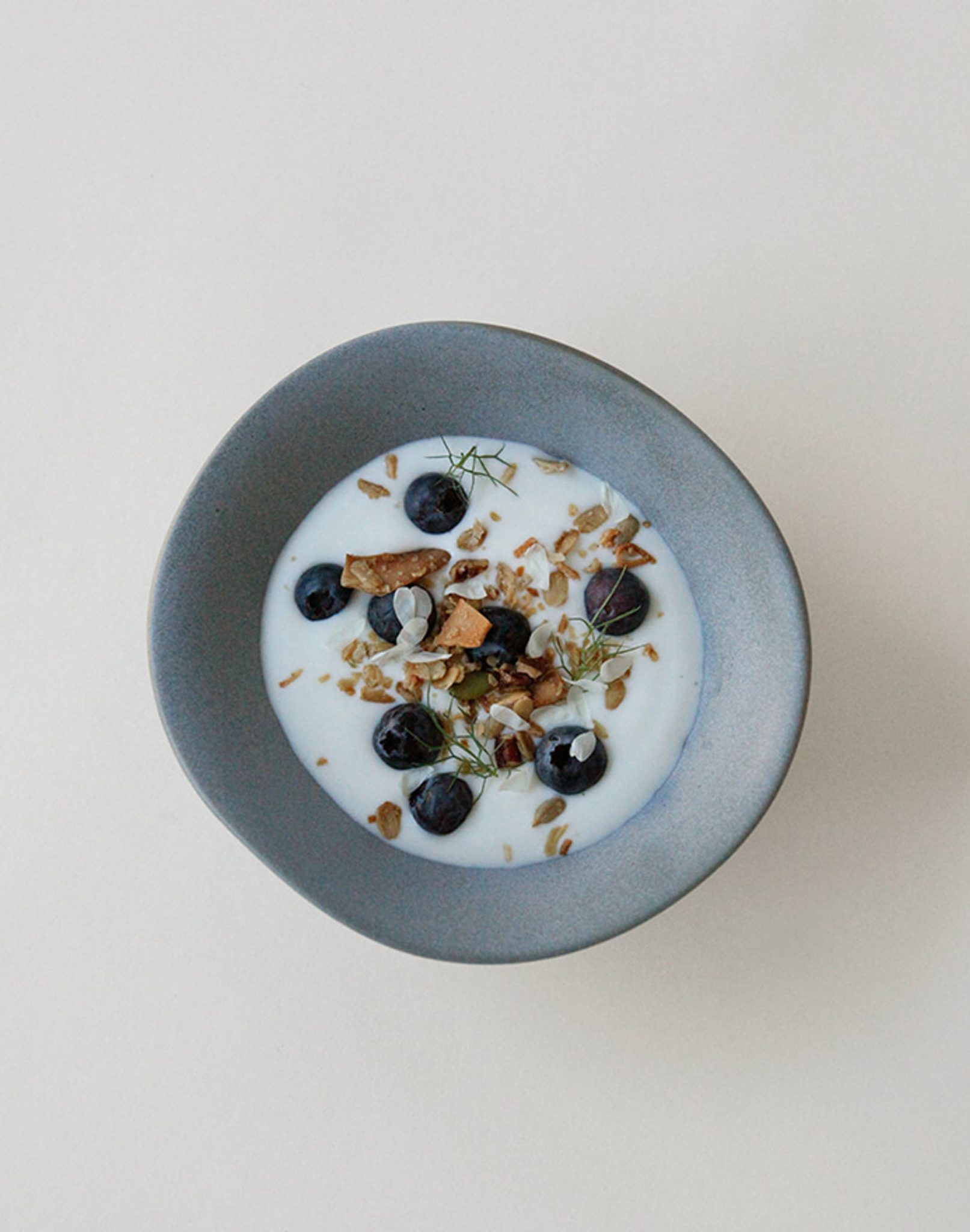 An NR Ceramics HIN Soup Bowl in gray, filled with yogurt, blueberries, granola, seeds, and green herbs on a neutral background—showcasing NR Ceramics versatile HIN tableware for any occasion.