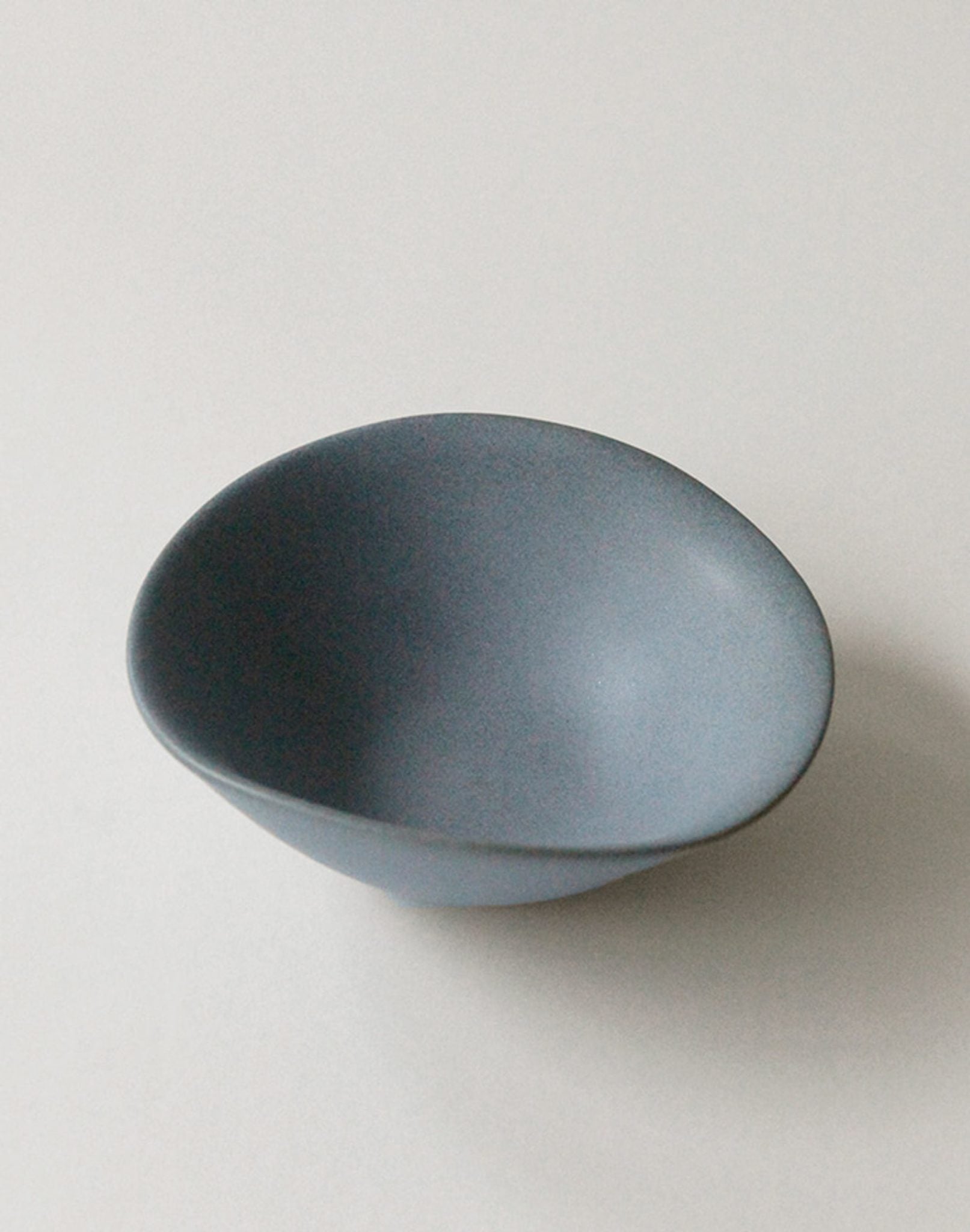 The NR Ceramics HIN Soup Bowl, a small and smooth asymmetrical blue piece, is displayed on a plain white surface, highlighting the versatile tableware design by NR Ceramics.
