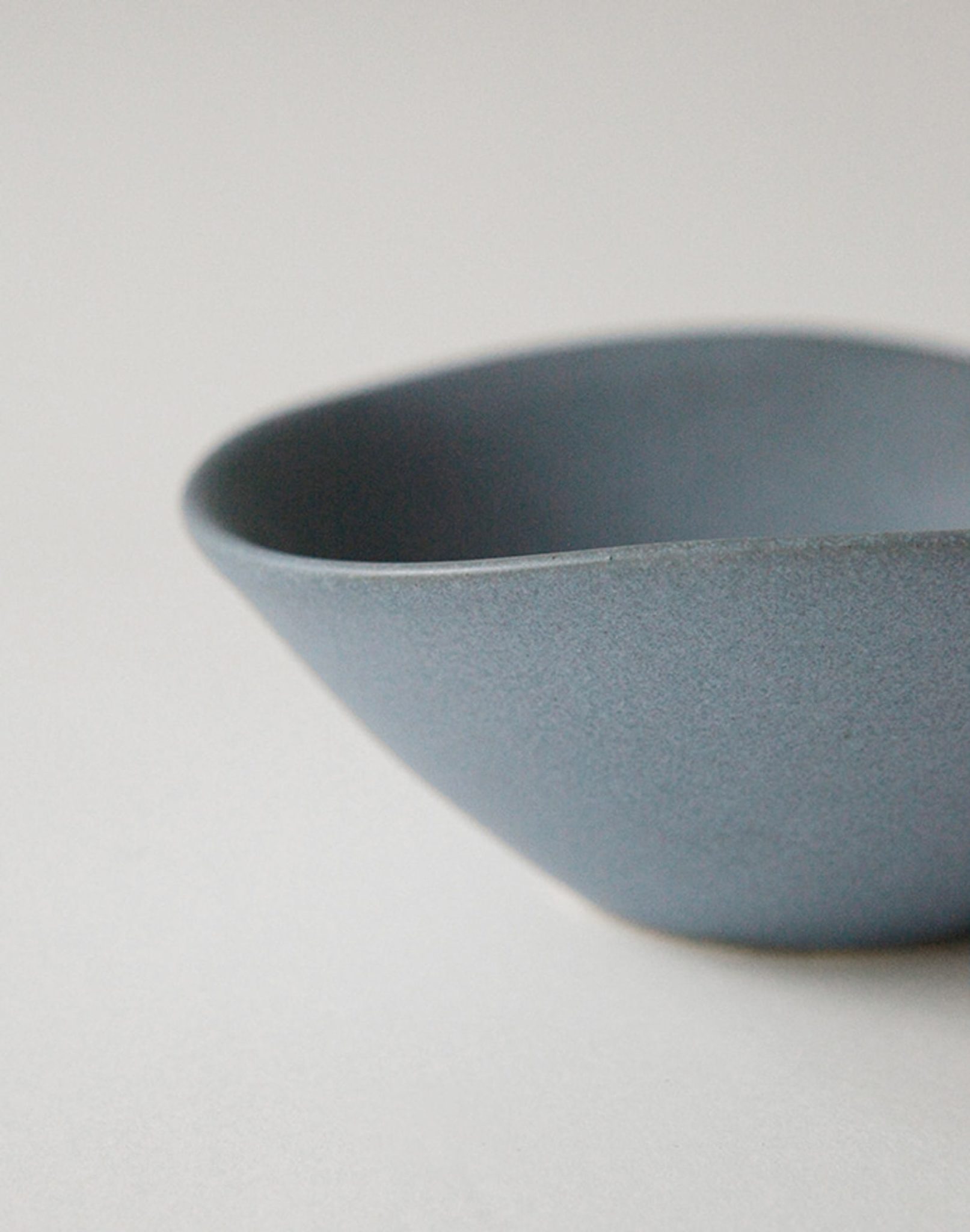 A close-up of the NR Ceramics HIN Soup Bowl, a minimalist blue ceramic bowl with a matte finish and smooth, curved edges by NR Ceramics—an ideal, versatile tableware piece for any setting.